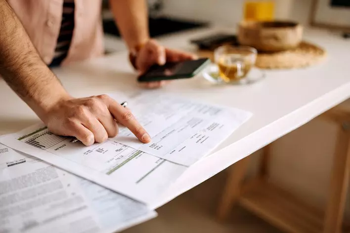 Man using a calculator on the phone to calculate expenses atop a table with a glass of tea