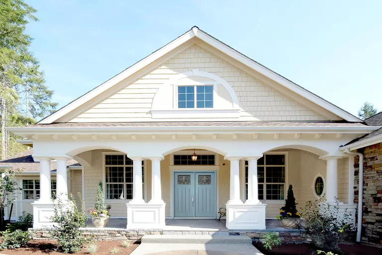 Front of a home with white shakes and large arches on the front porch.