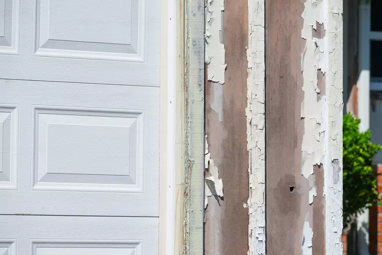 Chipped paint on the exterior wall of a house next to a garage door.