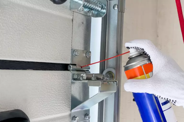Person spraying lubricant into the hinges of a garage door.