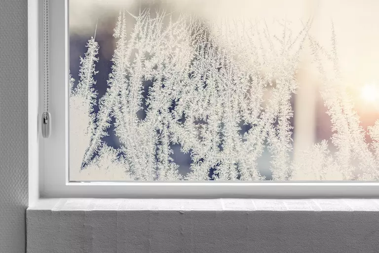A white window frame with ice forming on the glass.
