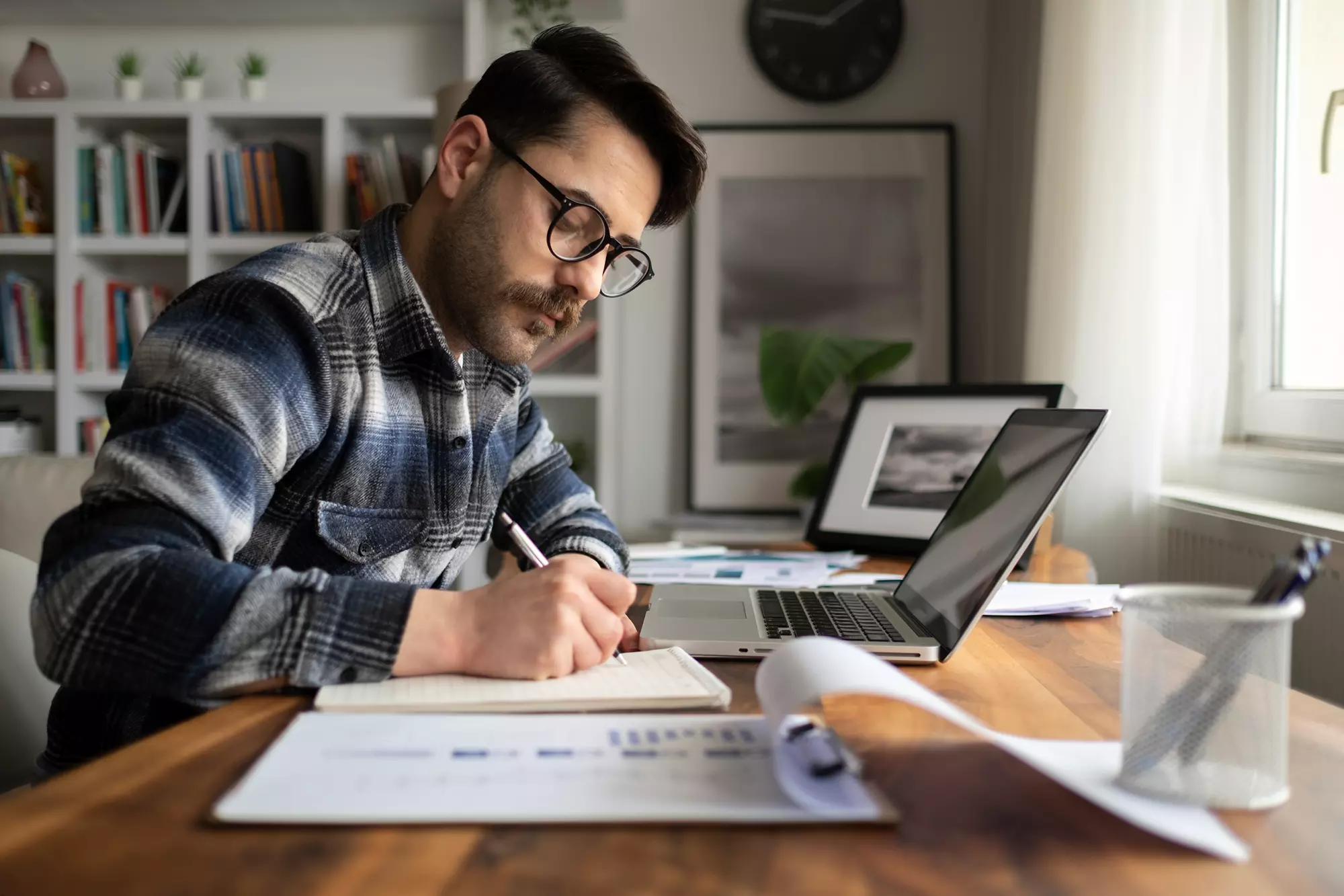 Man writing on a notepad in front of a laptop.
