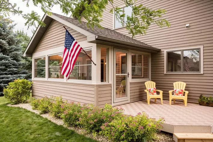 A tan-colored home with a back sunroom. The sunroom has a storm door, and there is patio furniture nearby on the exterior of the home.