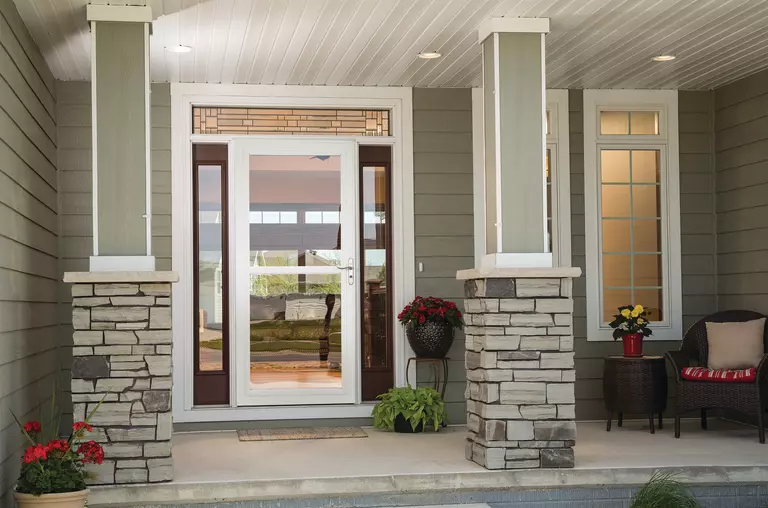 A home with two columns on its front porch and a traditional glass-front storm door that opens to a furnished porch.
