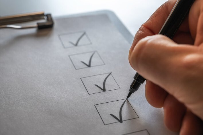A hand checking a row of boxes on a clipboard list to indicate completed steps in a DIY home remodel plan.