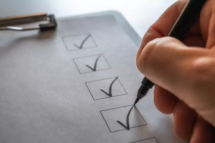 A hand checking a row of boxes on a clipboard list to indicate completed steps in a DIY home remodel plan.