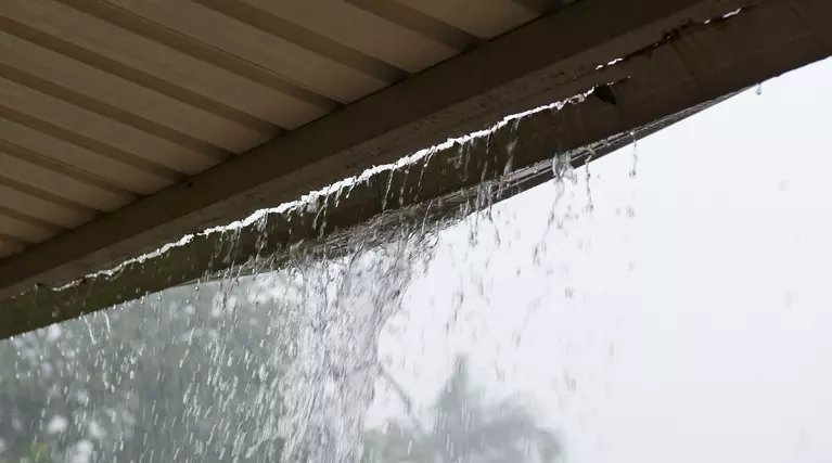 Gutters on a home that are visibly failing during a summer storm in which rain shows wear and tear.