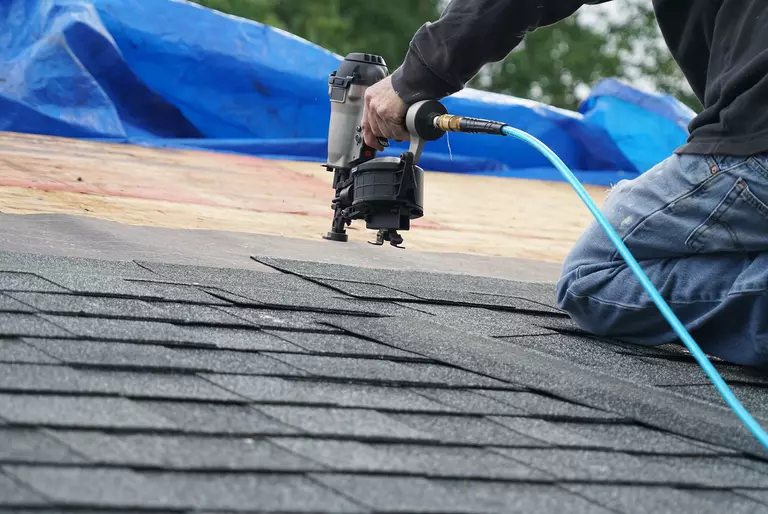 Worker using a roofing nailer to secure new roof shingles.