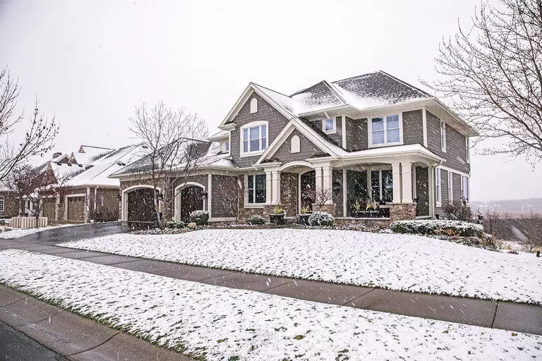 The front exterior of a home with tan siding during a snow shower.