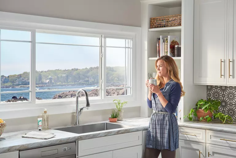 Person enjoying a cup of coffee in their kitchen while they look out their custom coastal windows.