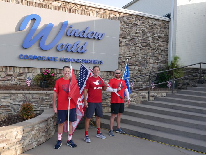 Three men standing in front of Window World Corporate headquarters sign, each holding up a flag &mdash; an American flag, a Window World flag, and a Team Red, White & Blue flag.