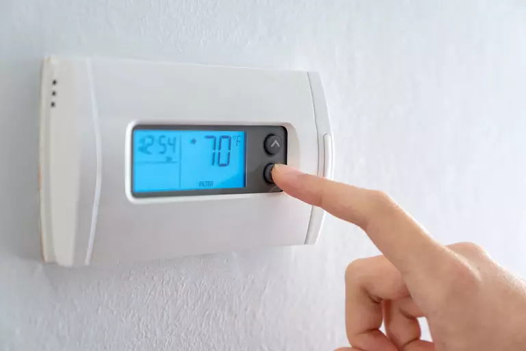 Person adjusting a digital thermostat on a wall.