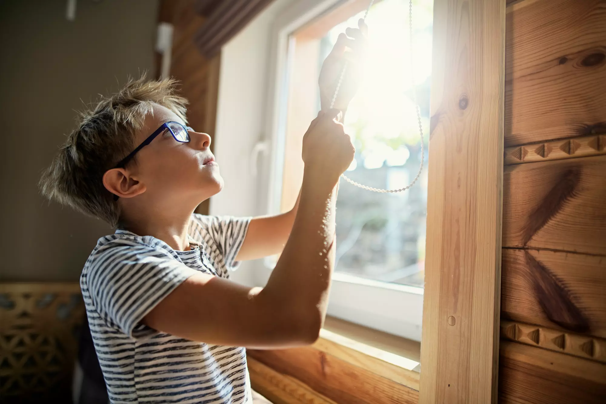 Boy adjusting the blinds in front of a window.