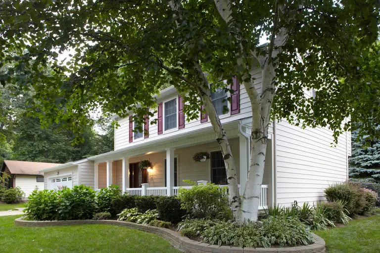The exterior of a house with white composite siding and red shutters.