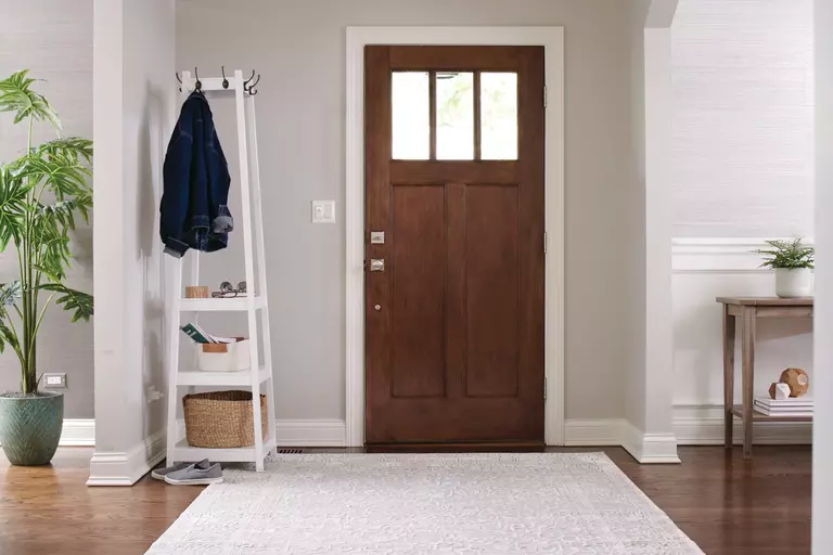 The living room and entryway of a home, with a brown vinyl entry door, a rack for jackets and keys, and neutral-toned decor encompassing the space.