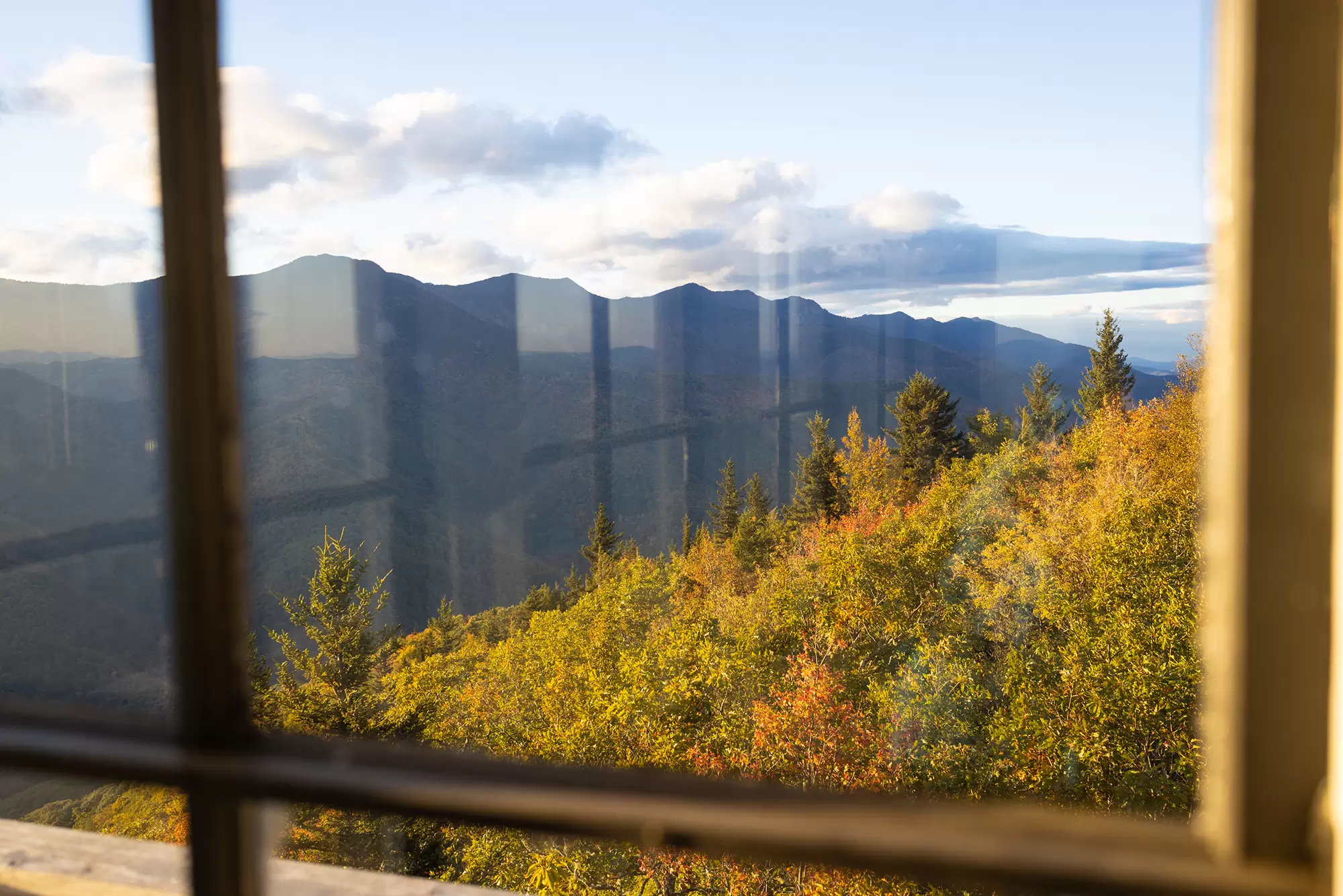 Mountain view with colorful fall foliage seen through a wood-framed window.