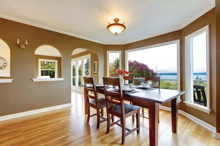 A dining room with a distant body of water visible through a set of bay windows.