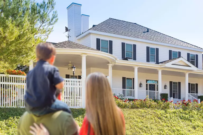 Family looking at beautiful home with white vinyl siding and a gray roof with gutter guard system.