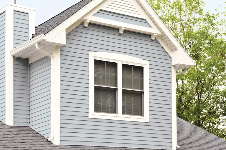 An upstairs section of a blue vinyl siding home with energy-efficient windows, clean gutters, and a well-maintained roof. 