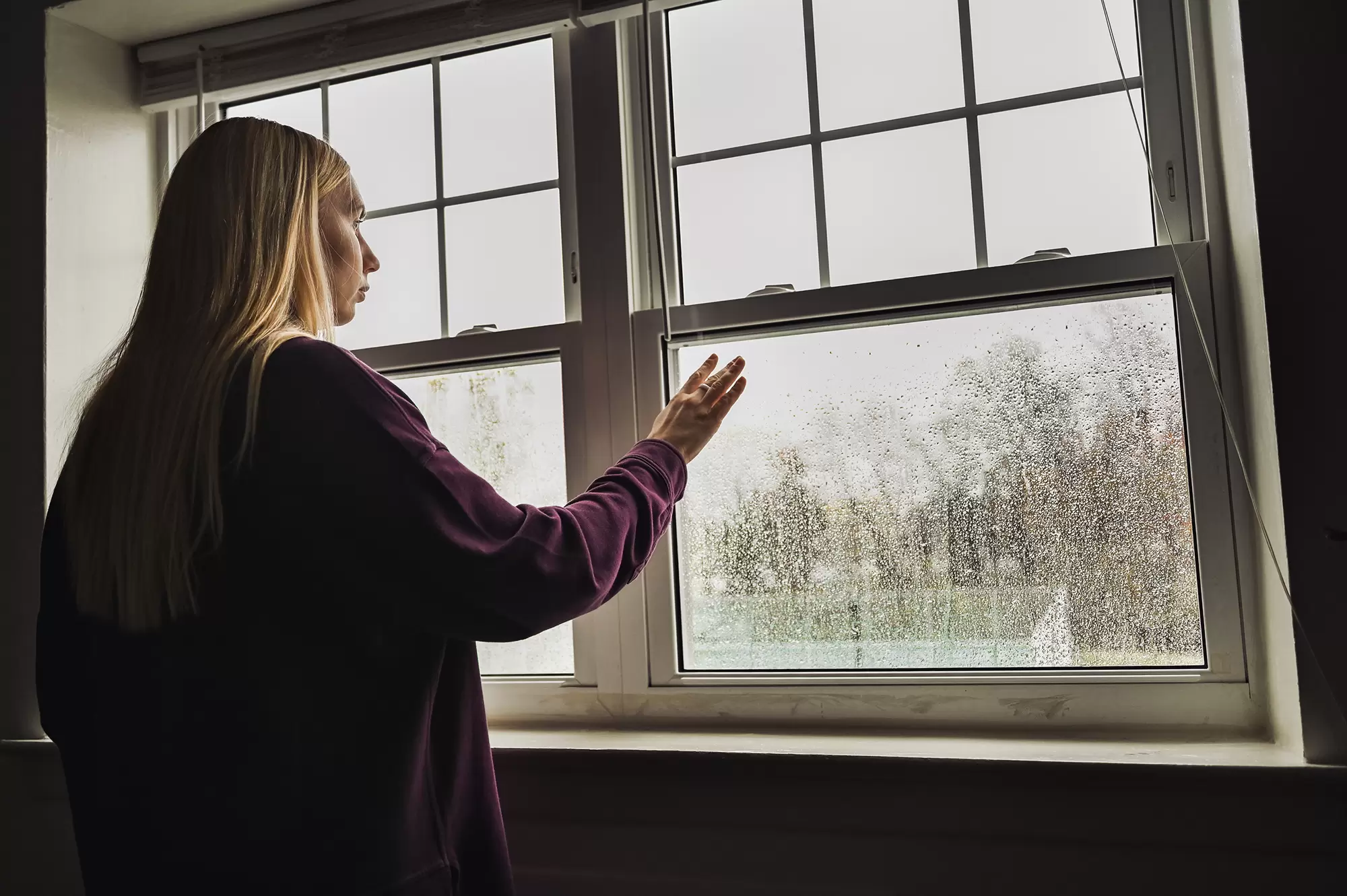 Woman touching a window with moisture on the pane.
