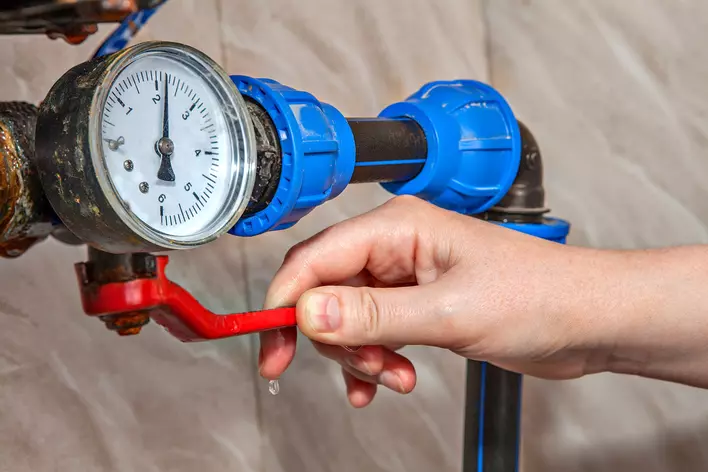 Someone checking the water pressure in a home with a water pressure gauge attached to the pipes.
