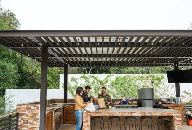 An outdoor kitchen in the back of a home, with family and friends eating together.