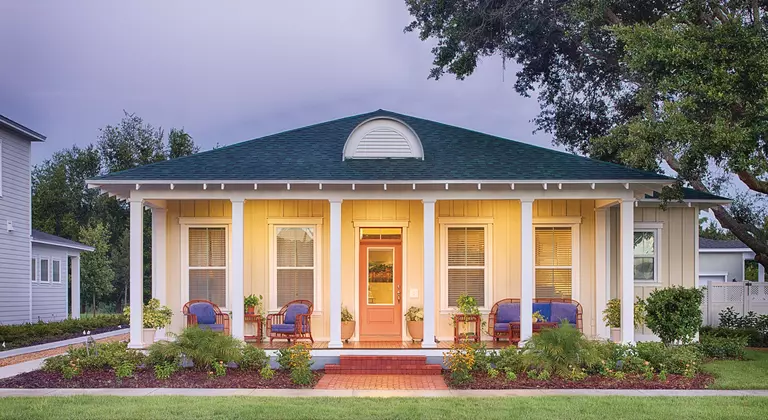 The front porch of a home at dusk with an orange front door.