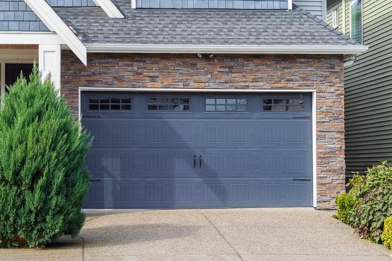 Navy steel garage door on a house with stacked stone and blue siding.