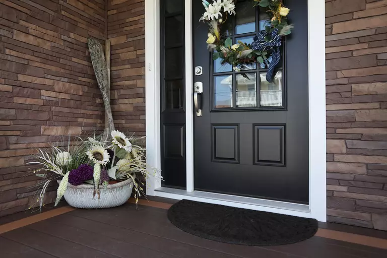 A black front door with a seasonal wreath and a basket of plants.