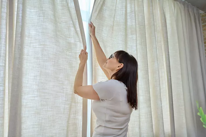 Woman closing the curtains in her home.