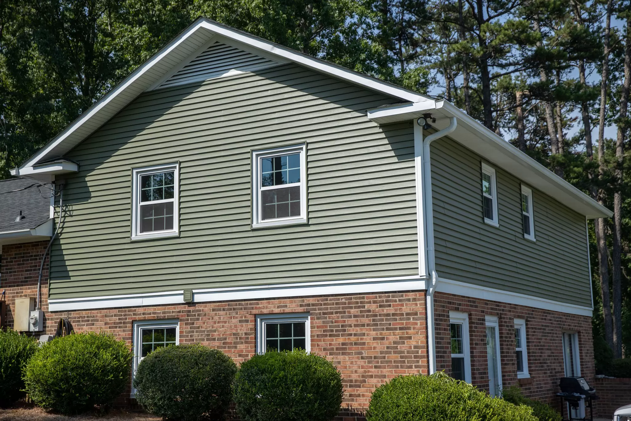 Home exterior with green vinyl siding and brick foundation.