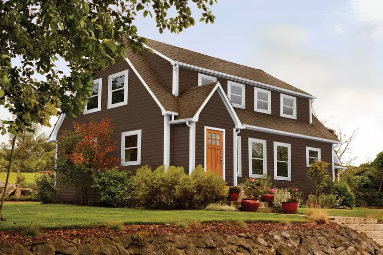 Front lawn of a home with dark brown siding and roofing featuring white windows.