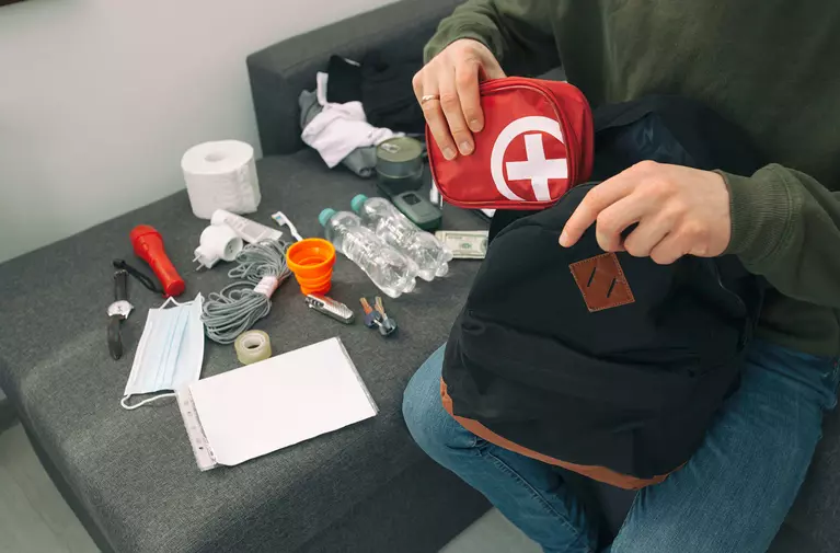 Man packing his backpack with an emergency kit and essentials to prepare for a hurricane. 