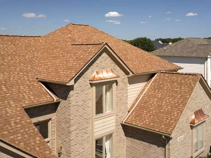 A tan brick home that has new wood shake roofing installed.