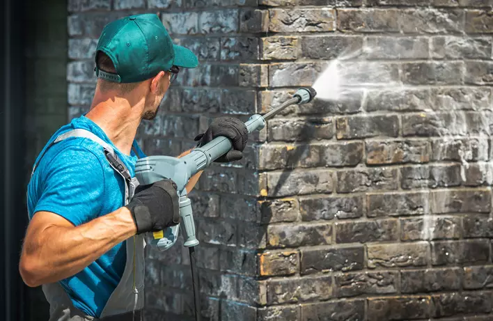 Man pressure washing brick exterior