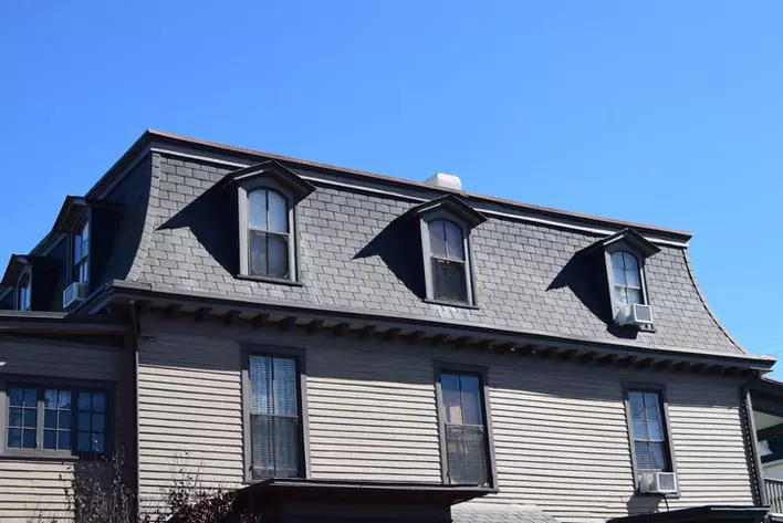 A dark-colored house with a mansard roof interspersed with dormer windows.