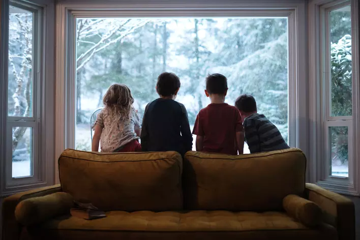 Children sitting in front of an energy-efficient bow window in Iowa looking at the snow outside