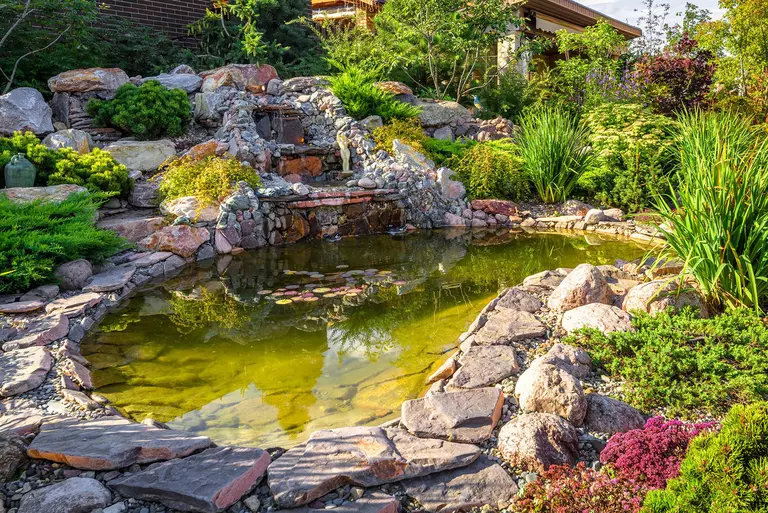 A multi-level fountain installed in the back patio of a home, made of stone and shrubbery to create a calm, cozy back patio space.