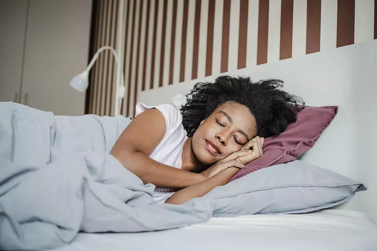 A woman sleeps on a bed in a naturally lit room.